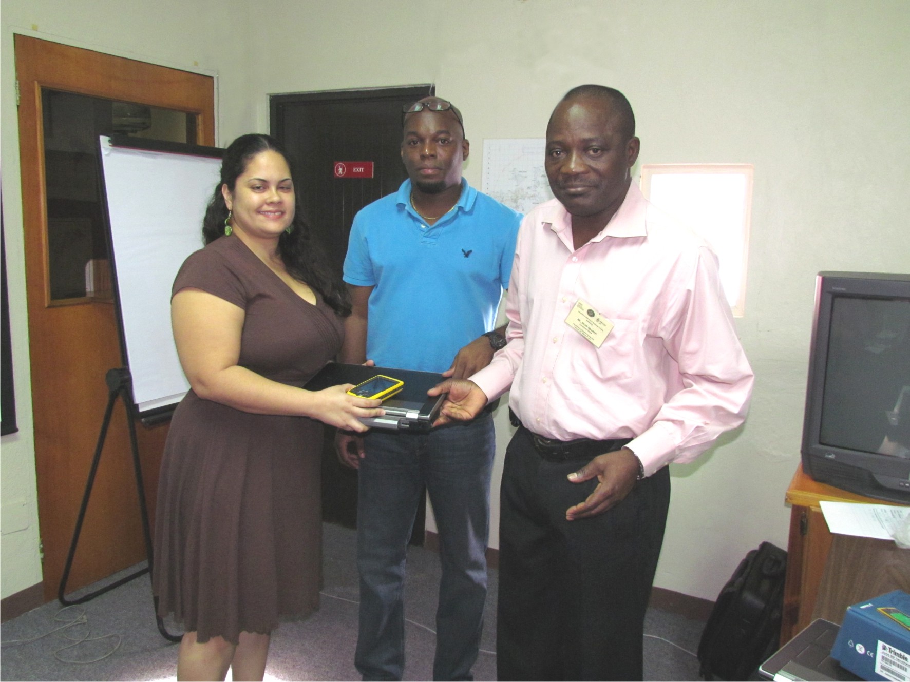 Dr. Jacob Opadeyi, Head of Geometrics Engineering and Land Management at the University of the West Indies, Trinidad and Tobago hands over Mobile ArcPad Computer and a JUNO handheld GPS system to Ms. Garymar Rivera, Senior Technical Planning Manager at the Department of Disaster Management, Virgin Islands. Mr. Seon Levius (middle), Information and Communication Technologies (ICT) Specialist Manager and representative from CDEMA was present during the presentation